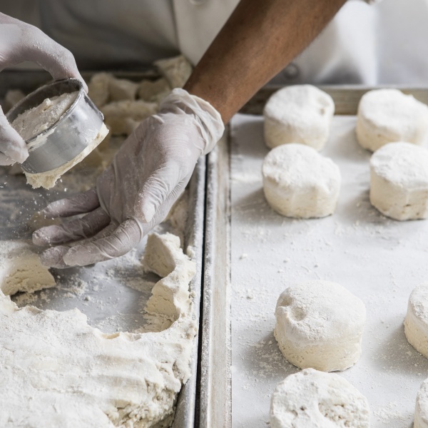 The hands of a baker punching out biscuit dough on a flour dusted sheet pan